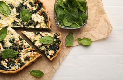 Delicious homemade quiche and fresh spinach leaves on white wooden table, flat lay