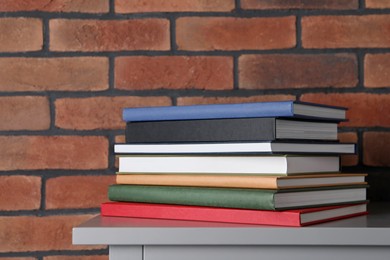 Stack of hardcover books on grey table near brick wall