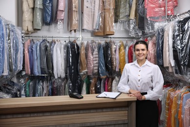 Photo of Dry-cleaning service. Happy worker at counter indoors, space for text
