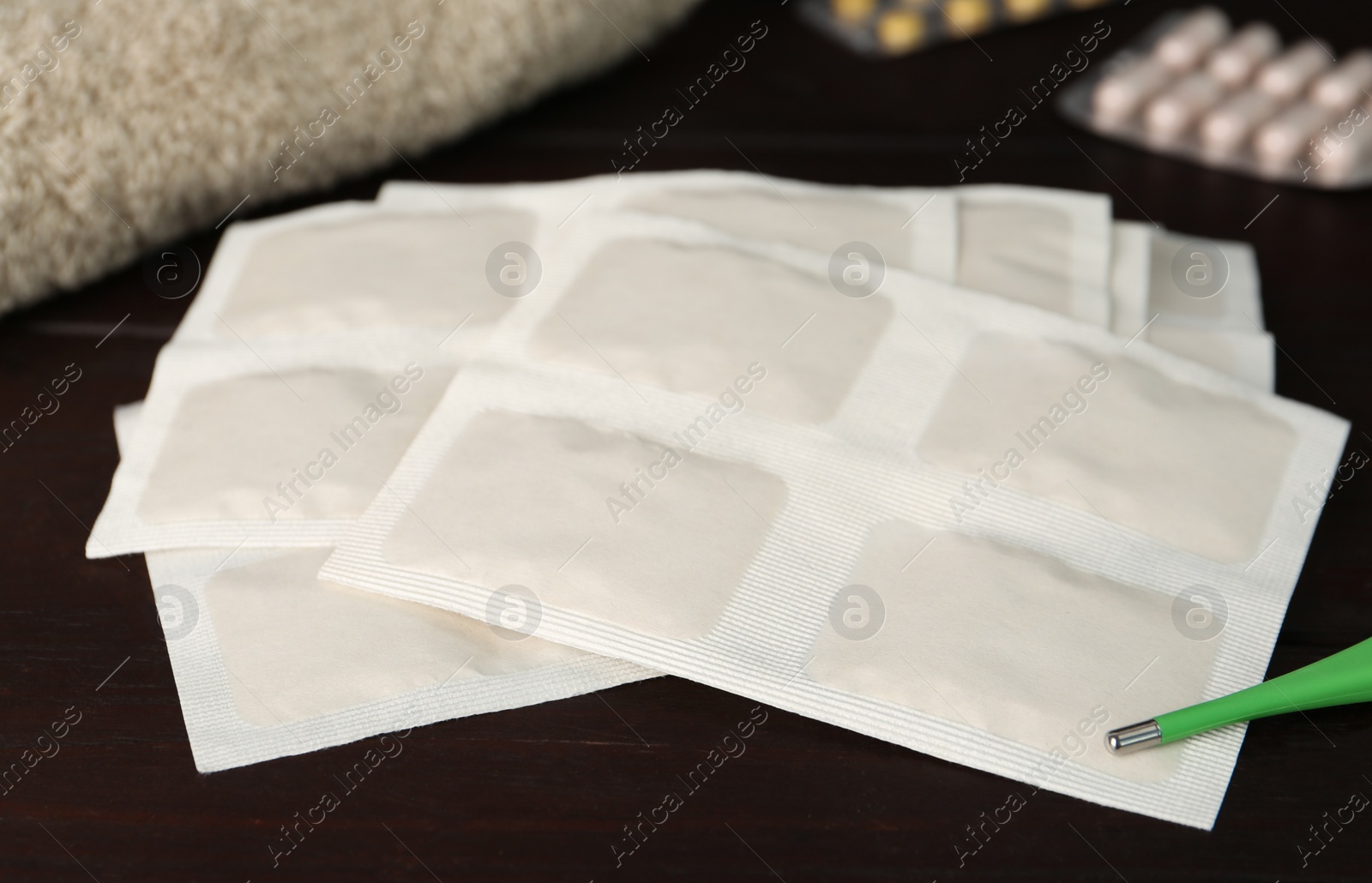 Photo of Mustard plasters, thermometer and pills on wooden table, closeup