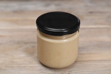 Photo of Tasty nut paste in jar on wooden table, closeup