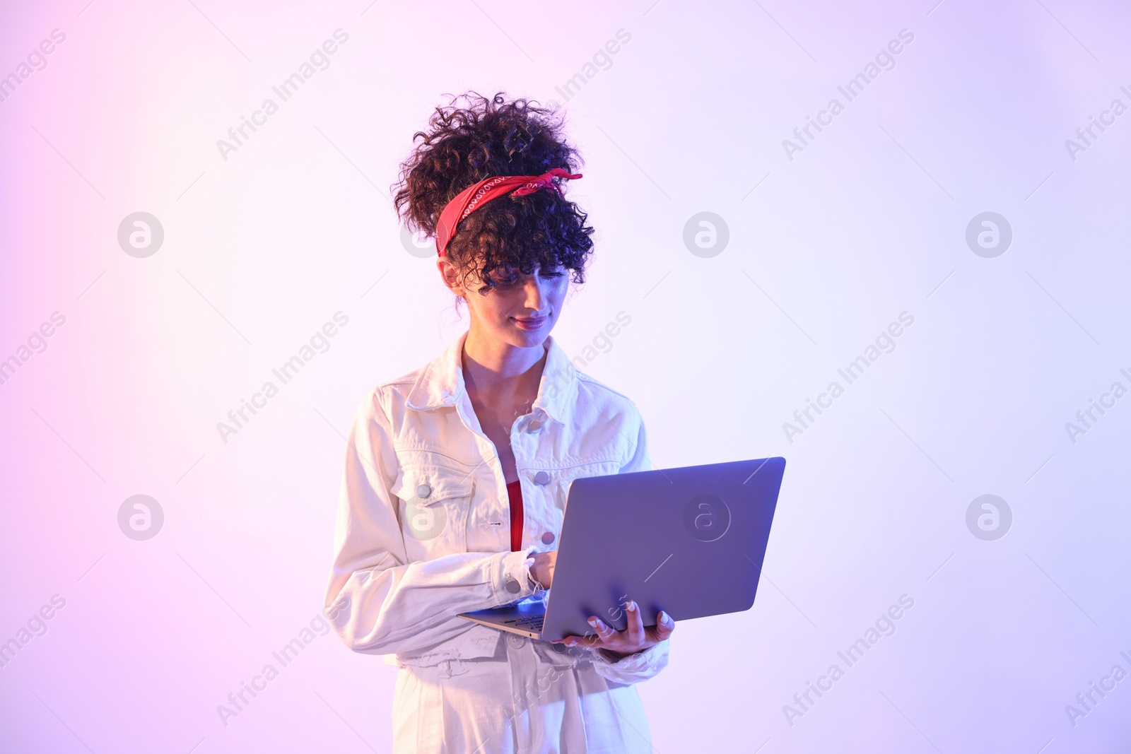 Photo of Beautiful young woman with laptop on color background in neon lights