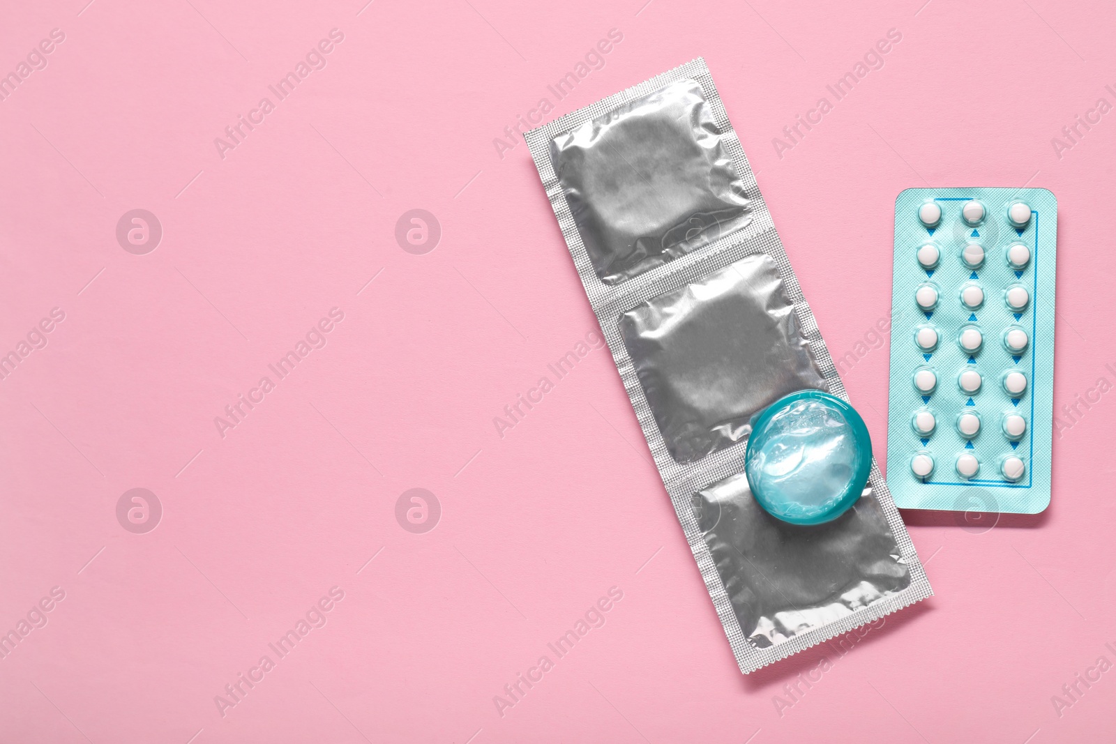Photo of Condoms and birth control pills on pink background, flat lay and space for text. Choosing method of contraception