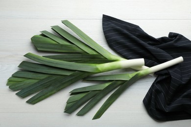 Fresh raw leeks and napkin on white wooden table, flat lay