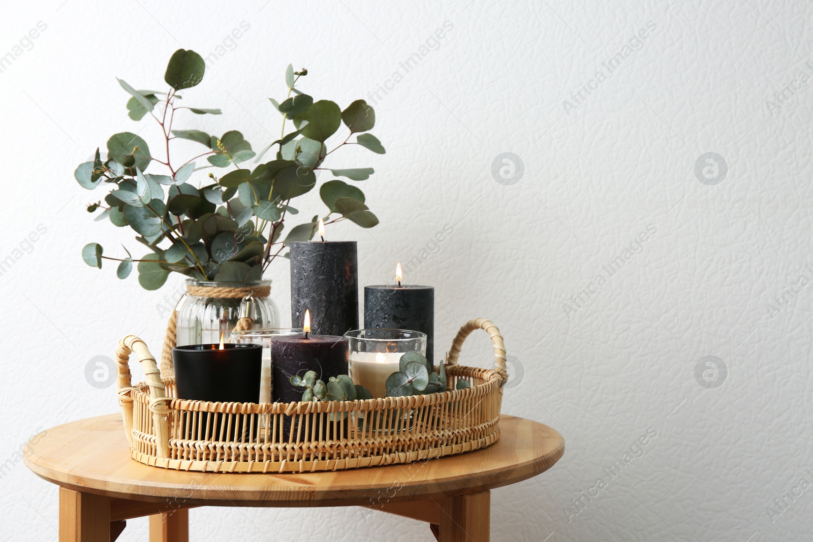 Photo of Tray with burning candles and green branches on table at white wall, space for text