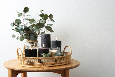 Tray with burning candles and green branches on table at white wall, space for text