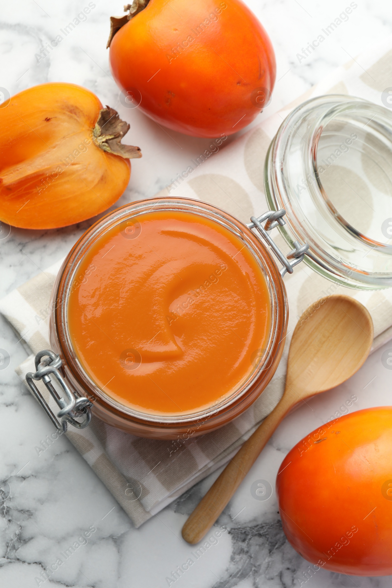 Photo of Delicious persimmon jam and fresh fruits on white marble table, flat lay