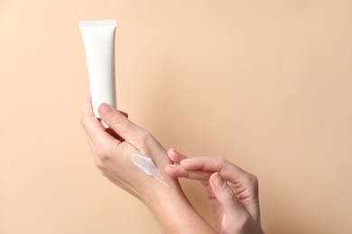 Woman with tube applying cosmetic cream onto her hand on beige background, closeup. Space for text