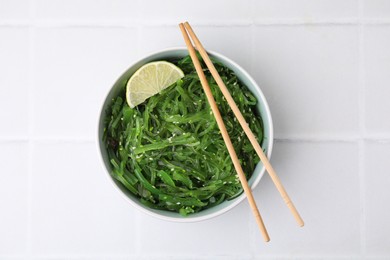 Photo of Tasty seaweed salad in bowl served on white tiled table, top view