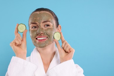 Photo of Beautiful woman with clay mask holding pieces of cucumber on light blue background, space for text