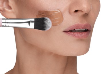 Photo of Woman applying foundation on face with brush against white background, closeup
