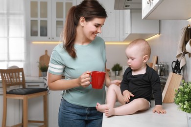 Photo of Happy young woman and her cute little baby spending time together in kitchen