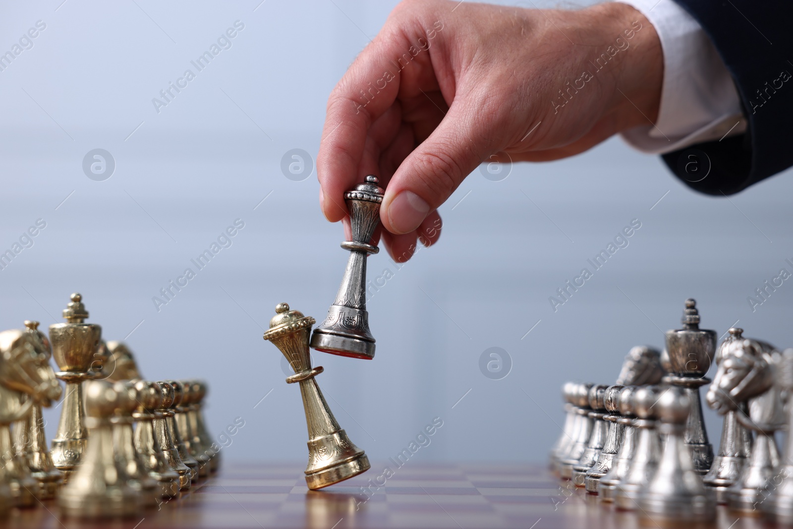 Photo of Man with bishop game piece playing chess at checkerboard against grey background, closeup