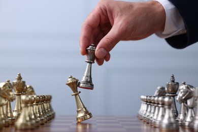 Photo of Man with bishop game piece playing chess at checkerboard against grey background, closeup