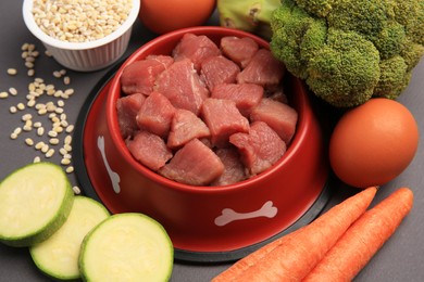 Raw meat in bowl and healthy products for pet on black background, closeup