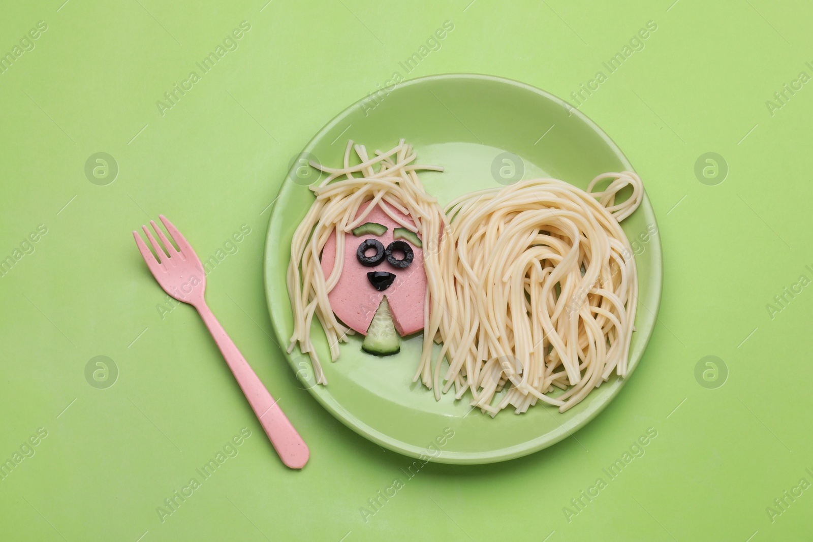 Photo of Creative serving for kids. Plate with cute dog made of tasty pasta, sausage and cucumber on green table, flat lay