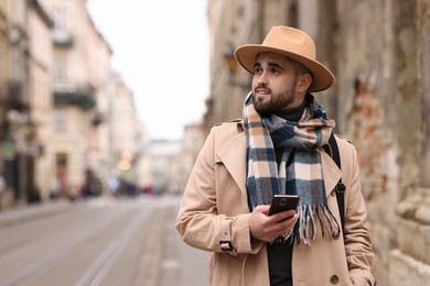 Photo of Handsome man in warm scarf with smartphone outdoors. Space for text