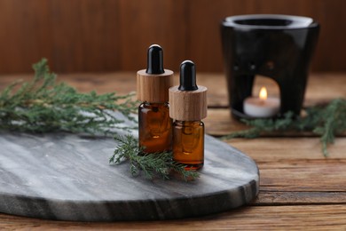 Bottles of juniper essential oil and twigs on wooden table