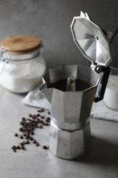 Brewed coffee in moka pot and beans on light grey table