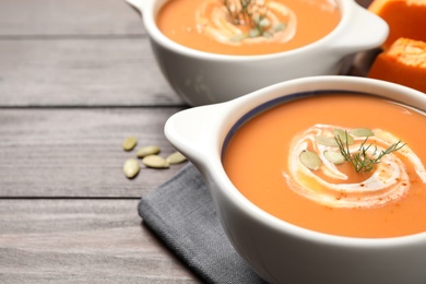Photo of Tasty creamy pumpkin soup with dill and seeds in bowl on wooden table. Space for text