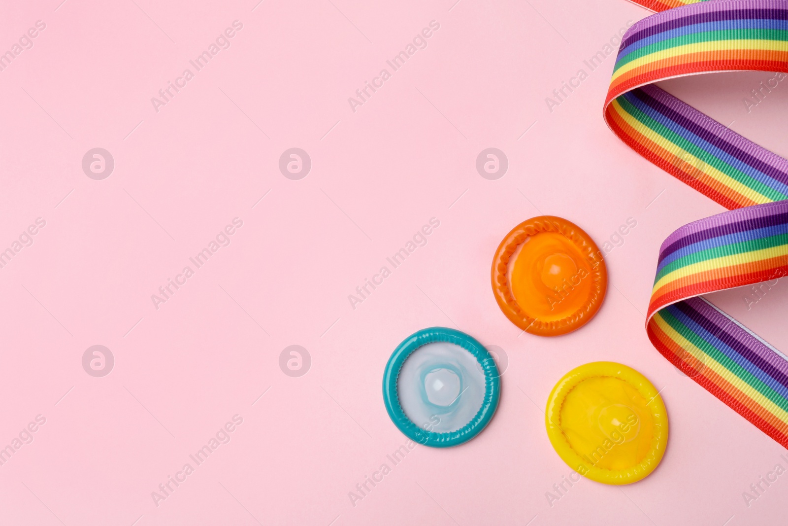 Photo of Flat lay composition with colorful condoms and rainbow ribbon on pink background, space for text. LGBT concept