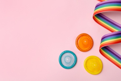 Photo of Flat lay composition with colorful condoms and rainbow ribbon on pink background, space for text. LGBT concept