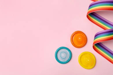 Flat lay composition with colorful condoms and rainbow ribbon on pink background, space for text. LGBT concept