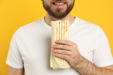 Young man with delicious shawarma on yellow background, closeup