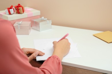 Photo of Young woman writing message in greeting card at white table, closeup