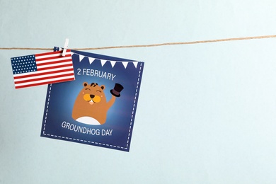 Photo of Happy Groundhog Day greeting card and American flag hanging against light background, space for text