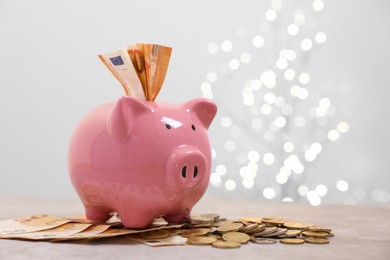 Photo of Piggy bank with euro banknotes and coins on grey table against blurred lights, space for text