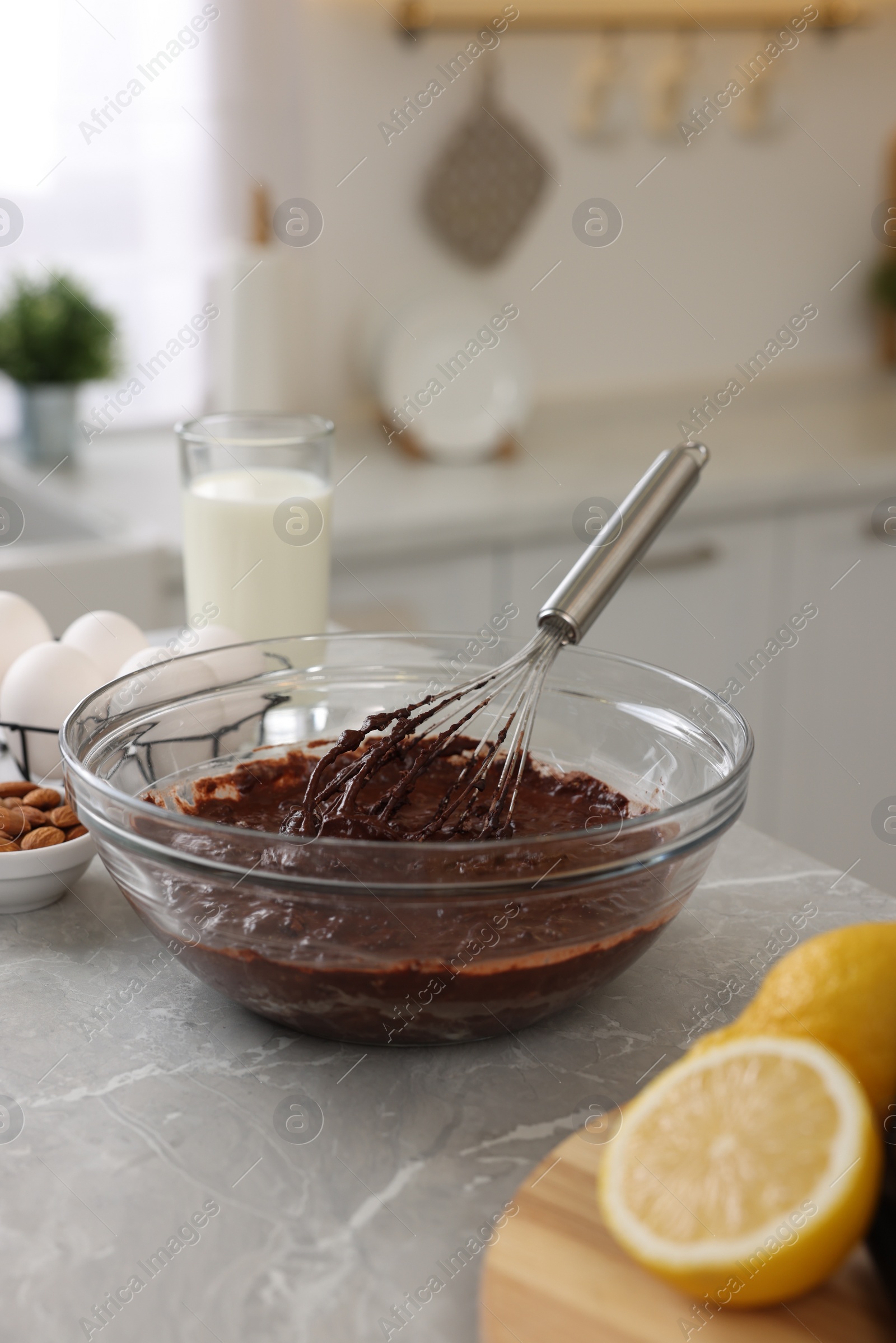 Photo of Metal whisk, chocolate cream in bowl and different products on gray marble table indoors