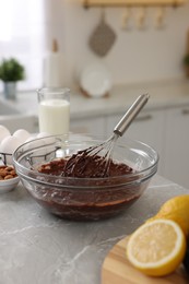 Photo of Metal whisk, chocolate cream in bowl and different products on gray marble table indoors