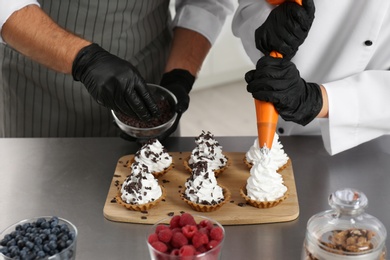 Photo of Pastry chefs preparing desserts at table in kitchen, closeup