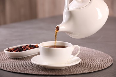Photo of Pouring aromatic tea into cup at grey table, closeup