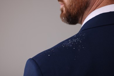 Man with dandruff on his suit against grey background, closeup. Space for text
