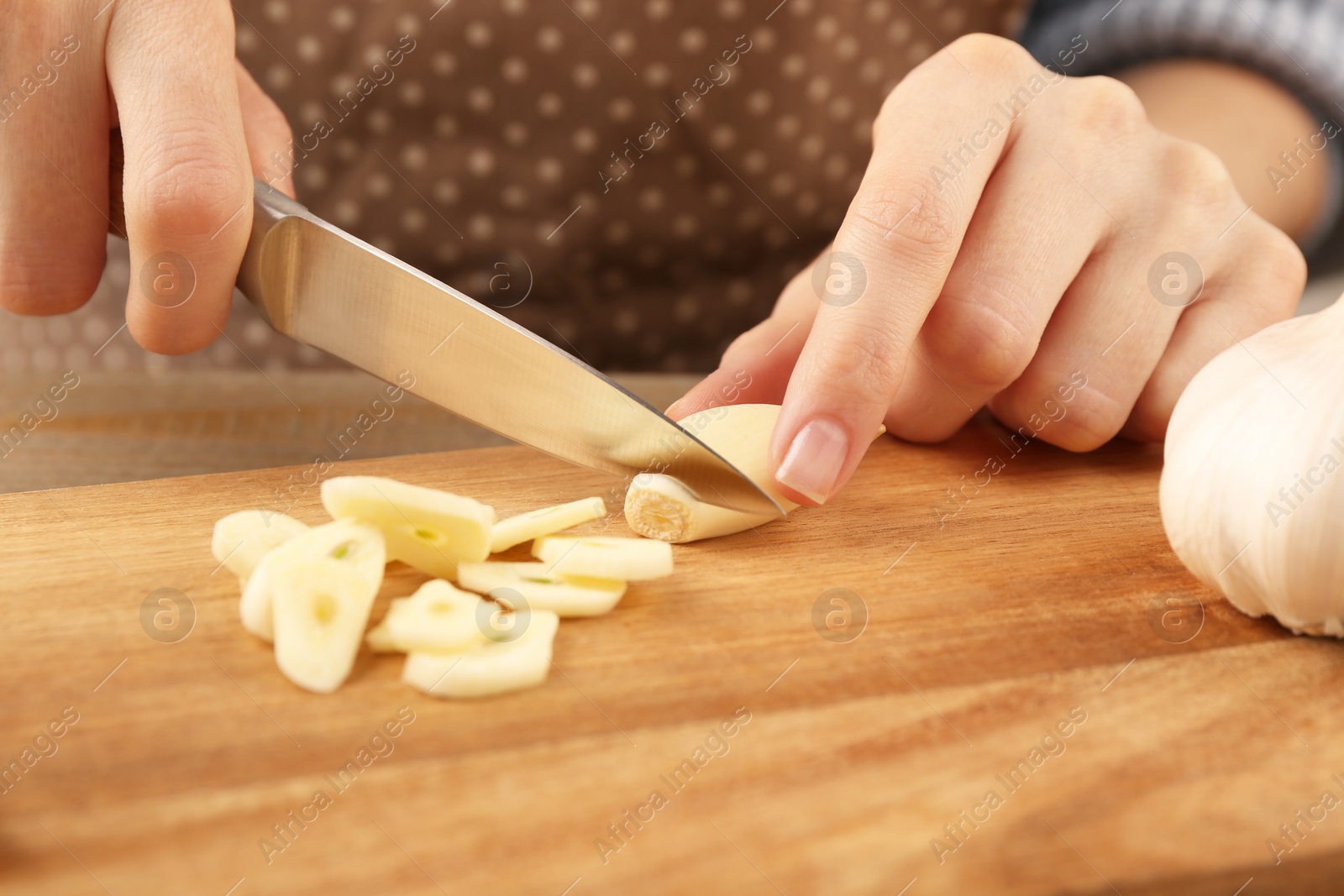 Photo of Woman cutting fresh garlic at table, closeup