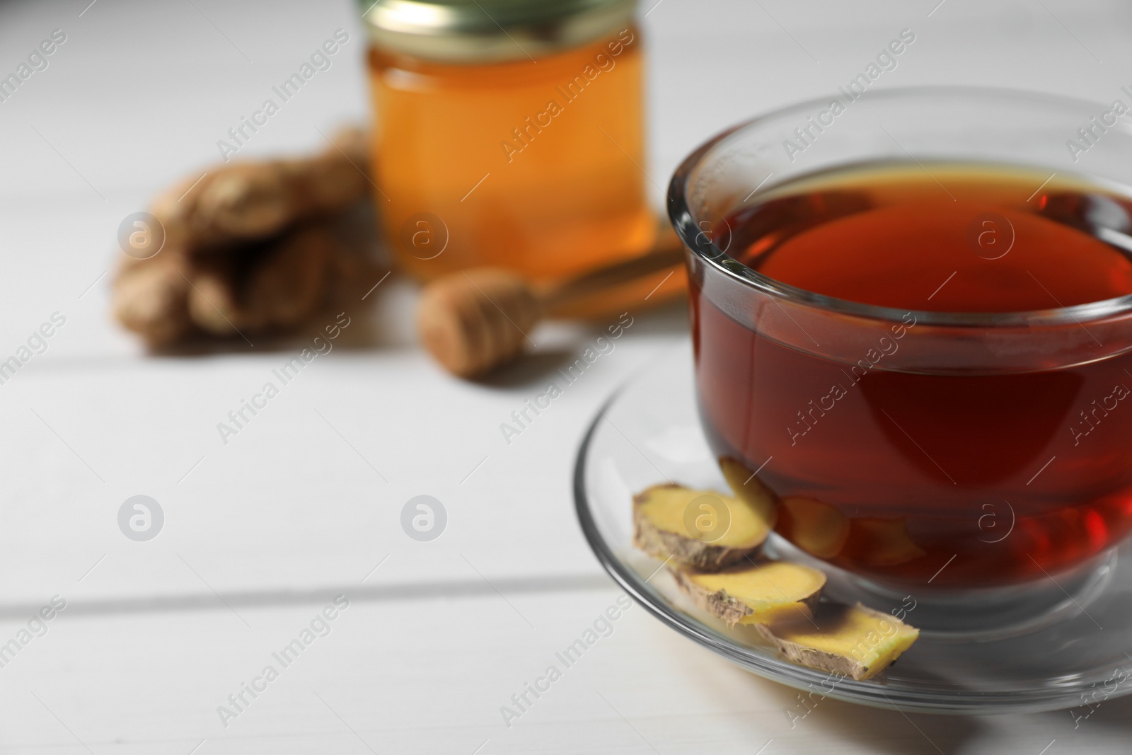 Photo of Cup of delicious ginger tea and ingredients on white wooden table, closeup. Space for text