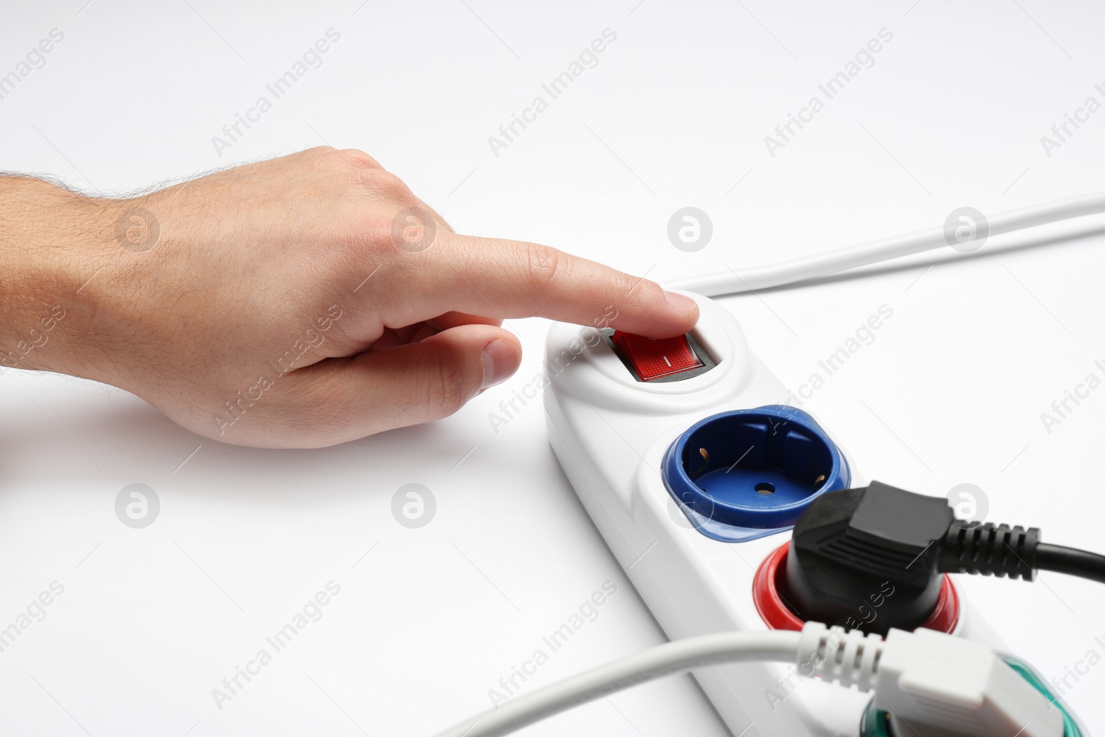 Photo of Man pressing power button of extension cord on white background, closeup. Electrician's professional equipment