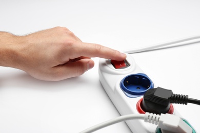 Man pressing power button of extension cord on white background, closeup. Electrician's professional equipment