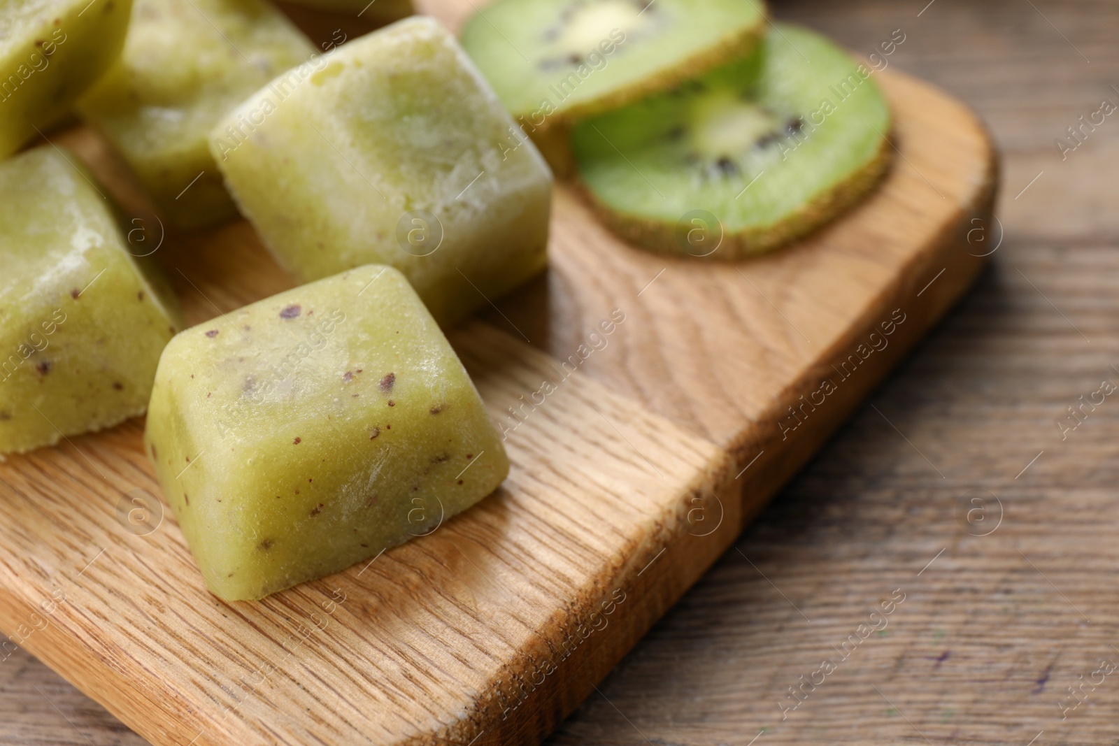 Photo of Frozen kiwi puree cubes and ingredient on wooden table, closeup