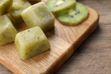 Photo of Frozen kiwi puree cubes and ingredient on wooden table, closeup