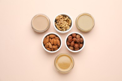 Different types of delicious nut butters and ingredients on beige background, flat lay