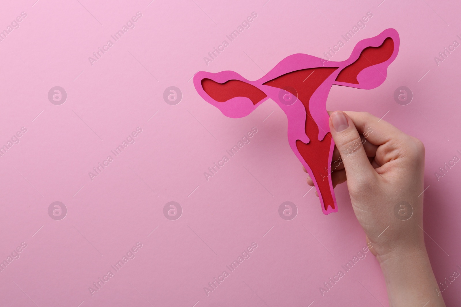 Photo of Reproductive medicine. Woman holding paper uterus on pink background, top view with space for text