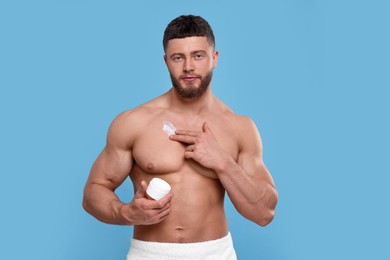 Handsome man applying body cream onto his chest on light blue background