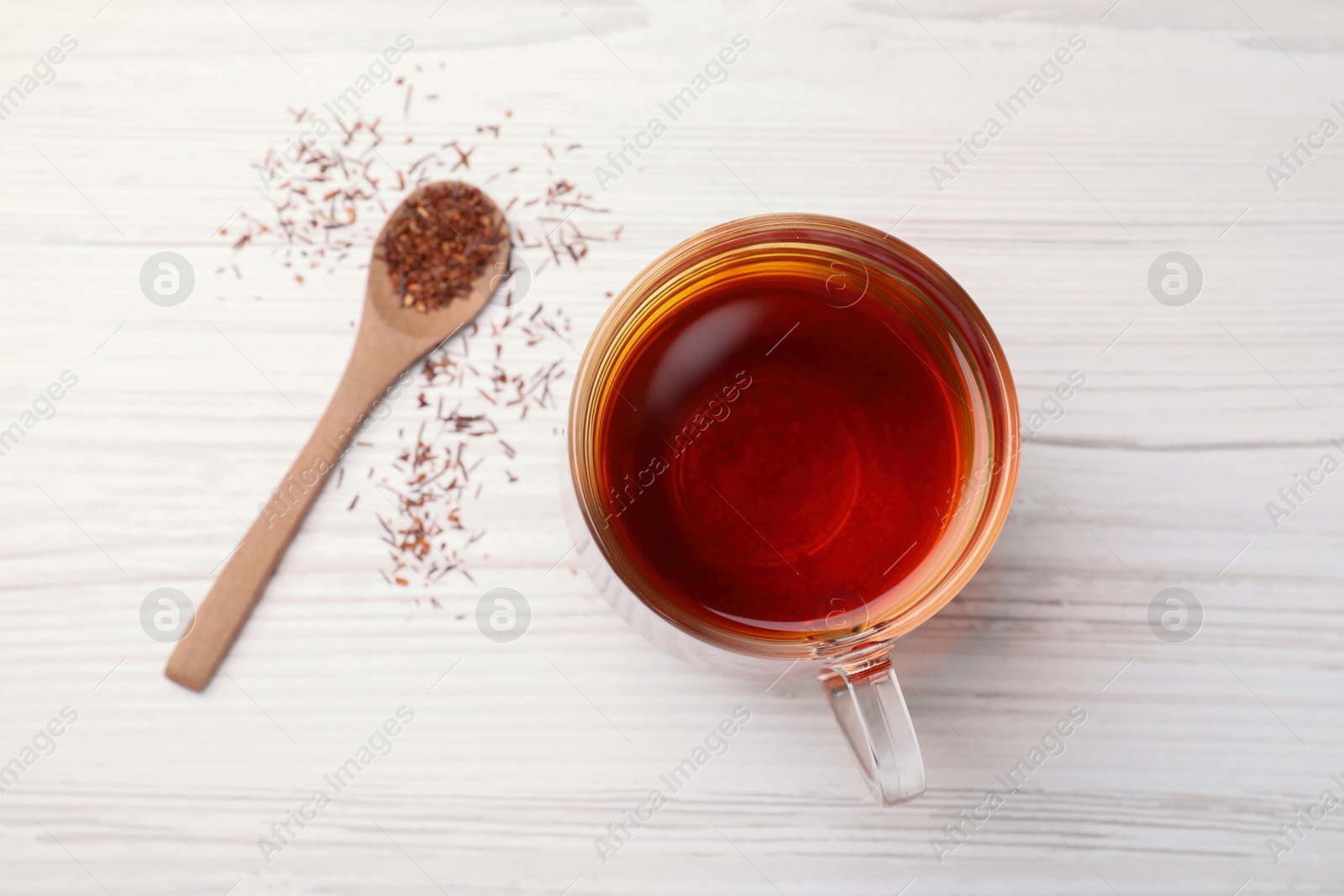 Photo of Freshly brewed rooibos tea, dry leaves and spoon on white wooden table, flat lay