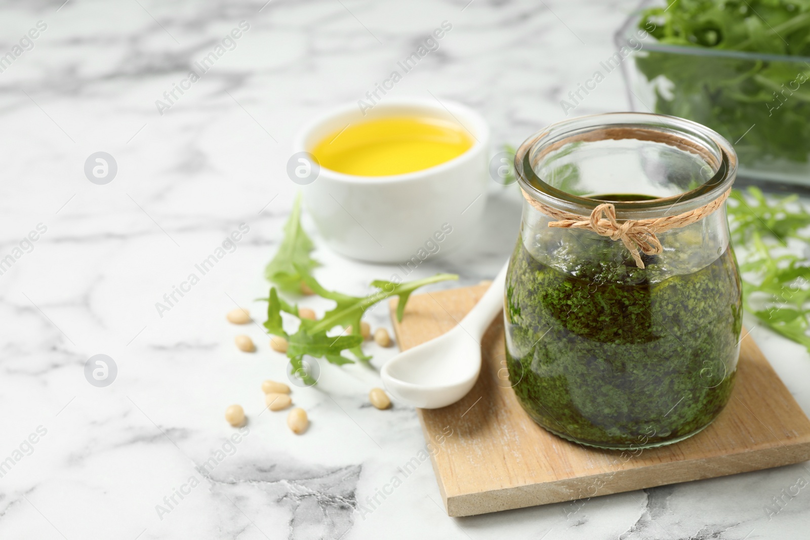 Photo of Jar of tasty arugula pesto and ingredients on white marble table