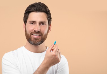 Handsome man with pill on beige background, space for text
