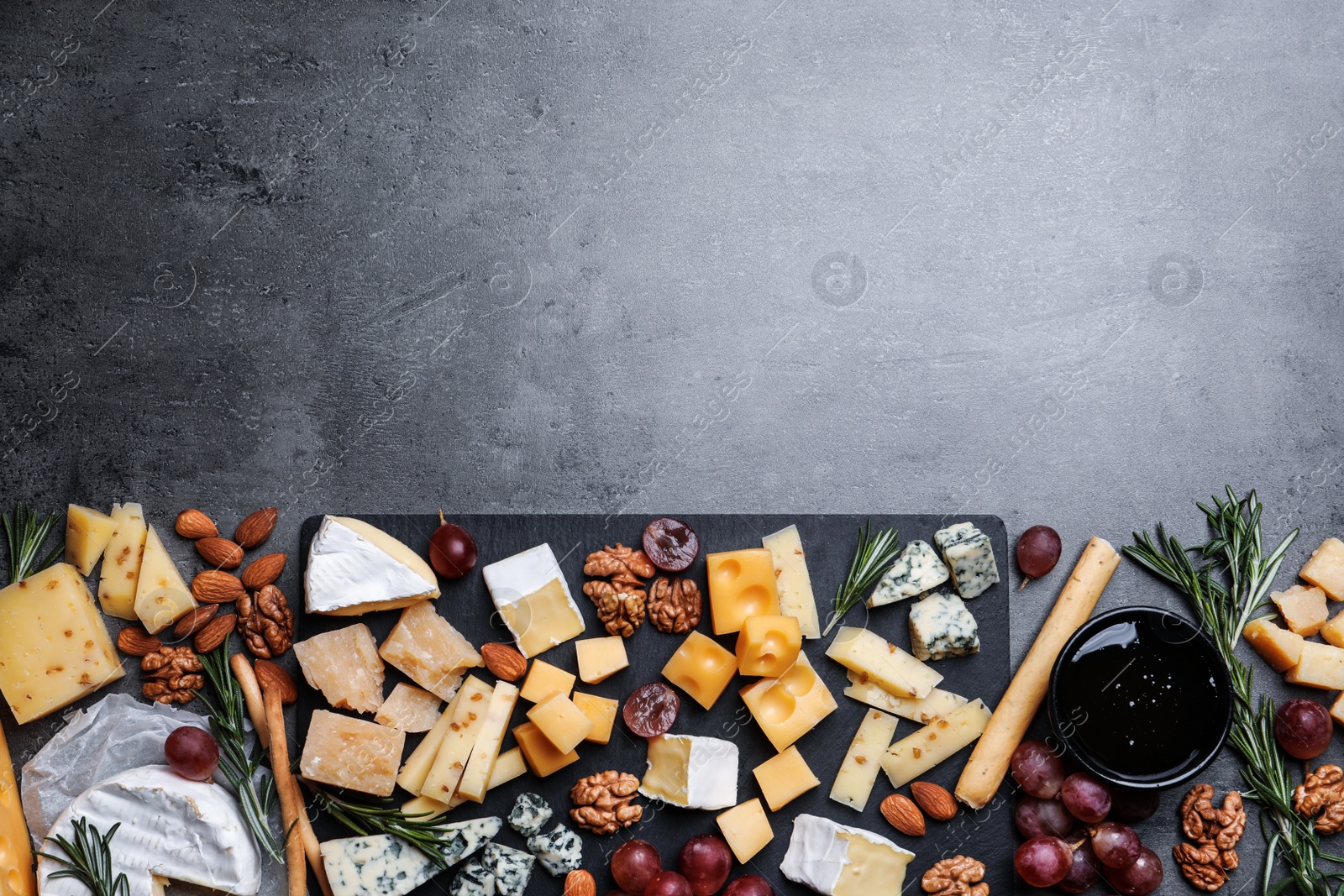 Photo of Cheese plate with grapes and nuts on dark table, top view. Space for text