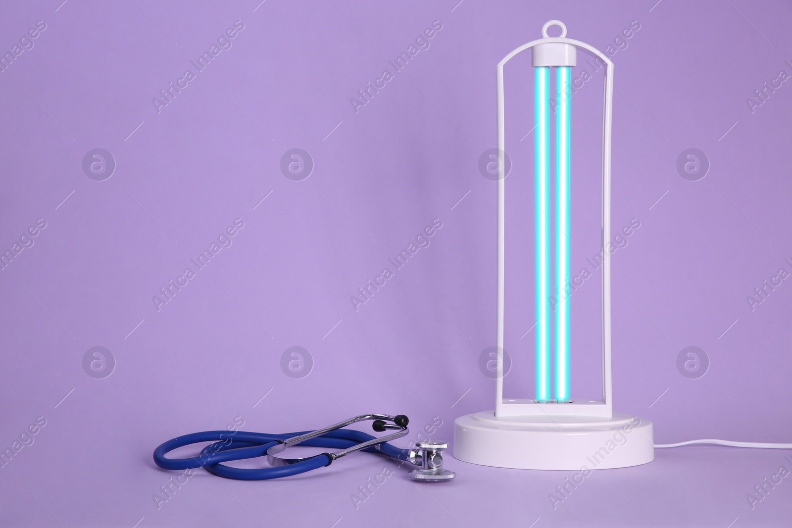 Photo of Ultraviolet lamp and stethoscope on violet background, space for text